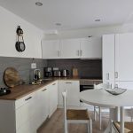 Helle Küche der Ferienwohnung 19a mit weißen Küchenschränken, dunkler Arbeitsfläche und Essbereich