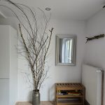 Heller Eingangsbereich der Ferienwohnung 19a mit dekorativen Zweigen, Schuhregal und Spiegel